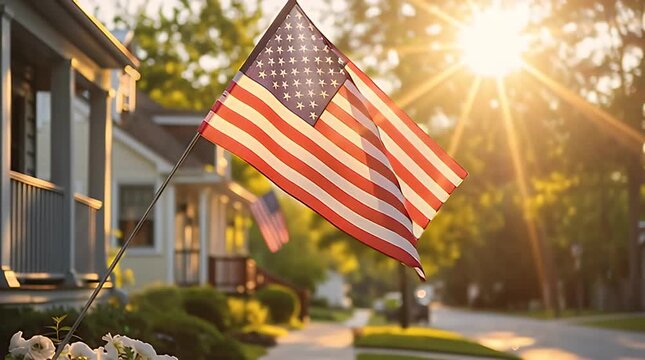 A beautifully sunlit American flag waves proudly attached to a residential home's porch railing during a bright summer day representing patriotism and national pride.