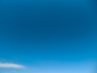 Obraz premium Blue sky with small airplane in flight above faint low clouds, conveying open space, freedom and travel, serene daylight atmosphere ideal for background or travel concept