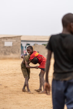 Two boys wrestling in the sand while another one is watching