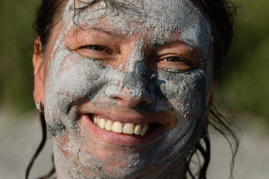 Smiling woman's face covered with blue clay