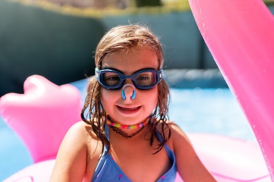 Young girl wearing nose clip and goggles smiling in a pool