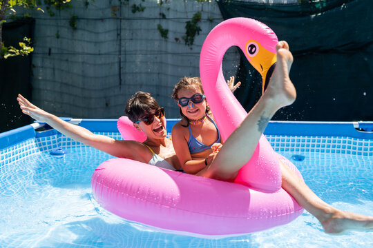 Mother and daughter having fun on inflatable flamingo in swimming pool