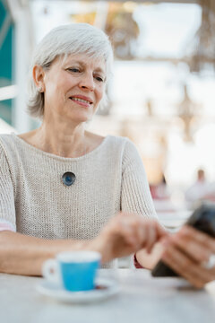 A woman uses her cell phone while drinking coffee in her free time