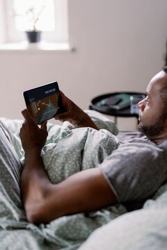 Cropped black man watching stock market graph on tablet on bed