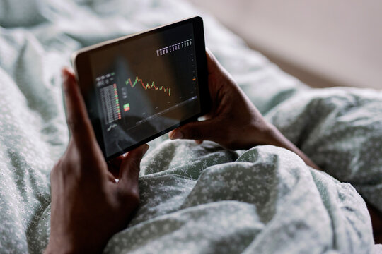 Partial black man watching business graph on digital tablet on bed