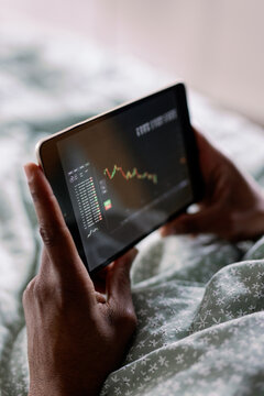 Cropped black man watching stock market graph on tablet on bed