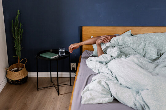 Man in bed reaching to table with water, smartphone and notebook
