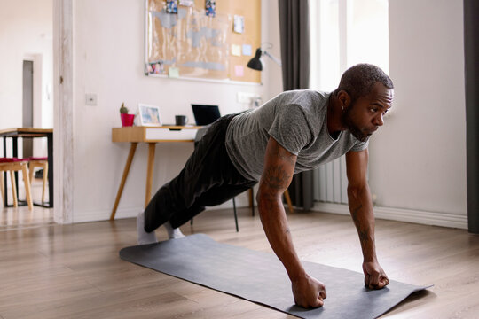 Concentrated adult black man doing push ups on fists on fitness mat