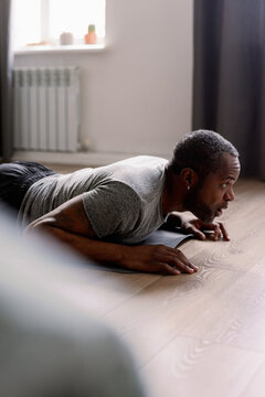 Adult man doing sport exercise on fitness mat in living room at home