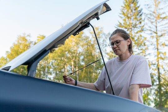 Woman Checking Car Oil with Dipstick Outdoors