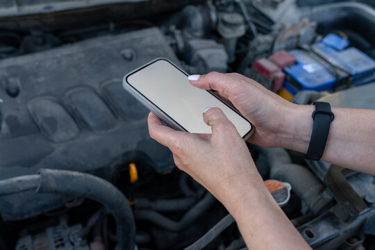 Hands using smartphone with car engine in background.