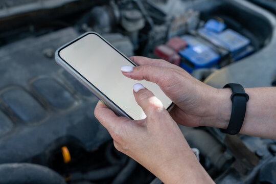 Close-up of hands using smartphone with car engine in background.
