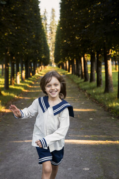 Child in a sailor outfit joyfully running through a tree-lined pathway