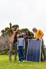 African American family standing on grassy lawn holding solar panel checking tablet and smartphone