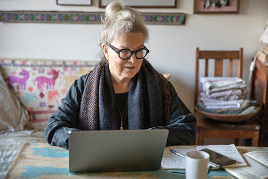Older woman at home with a laptop, coffee and notebook