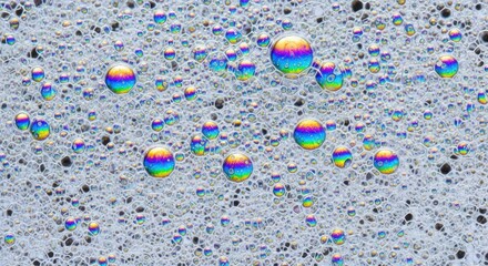 Rainbow-colored water droplets on a speckled gray surface viewed from directly above