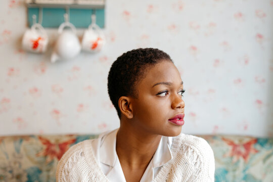Young Black woman sitting indoors with floral wallpape