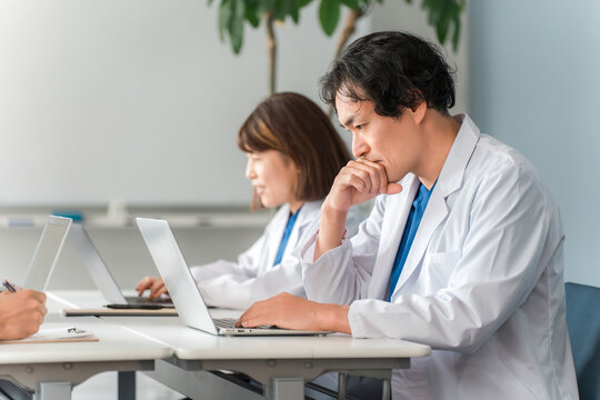 Male and female doctors in white coats sitting at desks and working