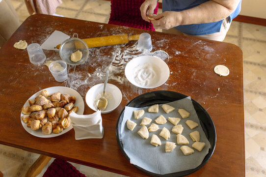 
hands of an elderly woman who places cookies on a baking sheet