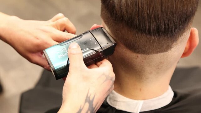 Stylist cutting man's hair with clipper in barbershop, closeup