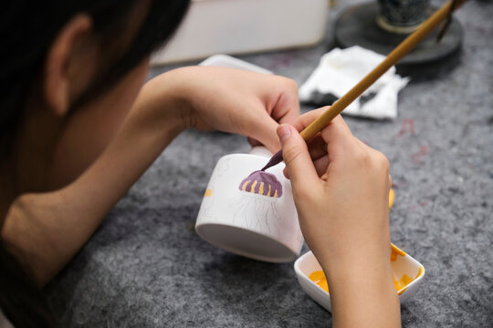 Asian girl painting on ceramic cup in studio