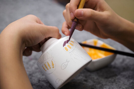 Asian girl painting on ceramic cup in studio, closeup
