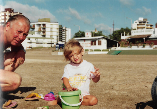Analog photo of grandfather and granddaughter playing in the sand