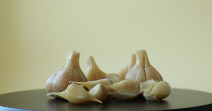 Pickled garlic bulbs and cloves on black table, closeup
