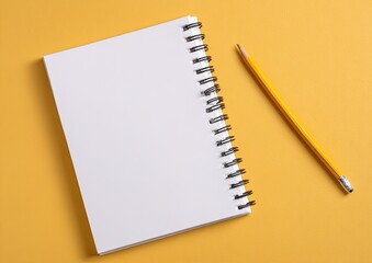Notebook with spiral binding and pencil lying on a flat, vibrant yellow surface