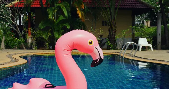Pink flamingo float by resort pool, wide view of blue tiled water with palm trees, pool chairs and cabana in background, serene luxury atmosphere and gentle ripples for holiday relaxation