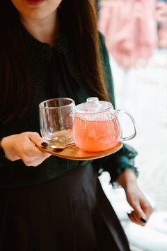 woman serving pink tea with glass teapot and cup on plate.