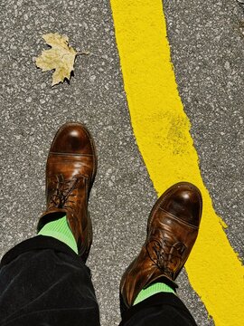 Leather shoes on a yellow road line with a dry leaf.