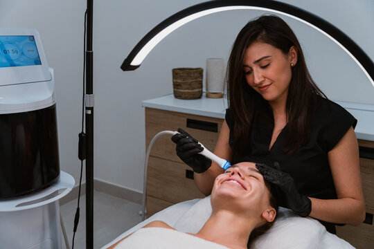 Beautician performing hydrafacial treatment on smiling woman