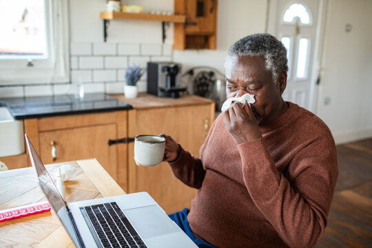 Older man with cold using laptop in home kitchen