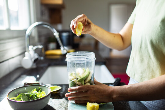 Person squeezing lemon into blender for green smoothie in home kitchen