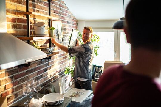 Man arranging frames on kitchen shelves at home
