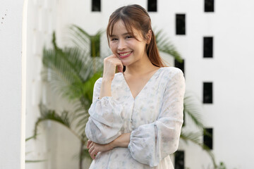 Portrait of cheerful beautiful asian woman wearing white stylish dress smiling at camera with hand...