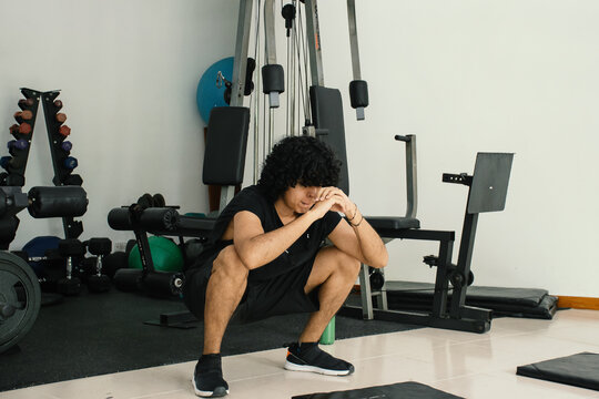 Young curly hair man squating at the gym