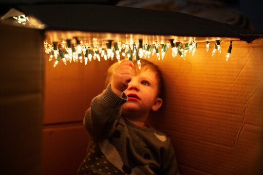 Child in cardboard fort with Christmas lights  
