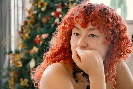 Curly readhead woman looking sideways in front of christmas tree