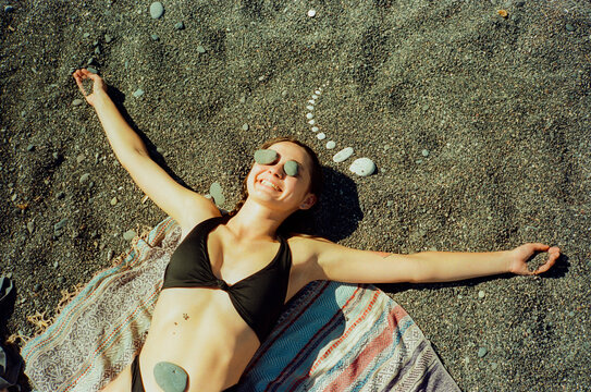 Woman laying on the beach sunbathing and warming with stones on her