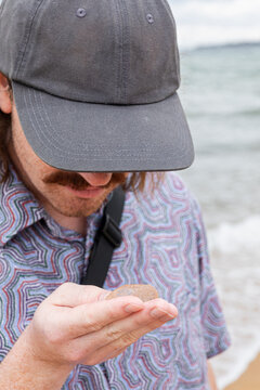 Man inspects a small object by the sea's edge closely in Australia
