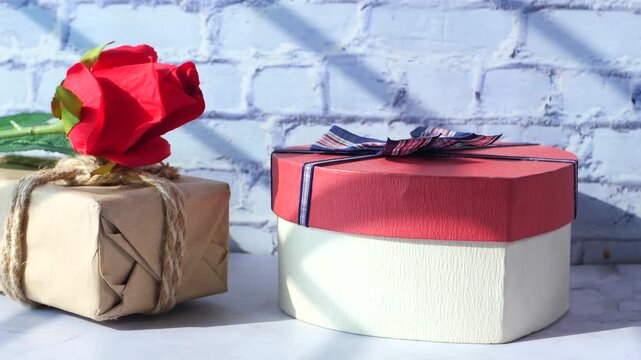 Heart shaped gift box and rose flower on white marble surface with cinematic sunlight and shadows