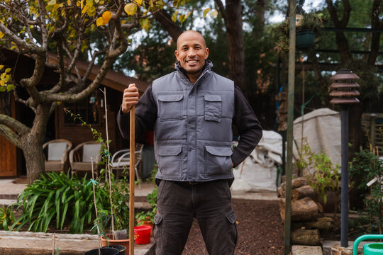 Happy Gardener Standing With Rake At Greenhouse