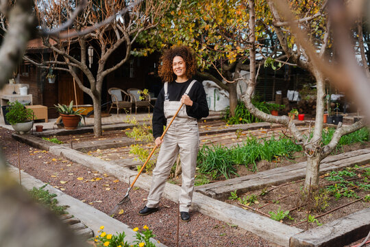 Smiling Woman Raking Garden In Greenhouse
