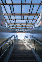 Obraz premium Ascending staircase in a metro station with glass roof and geometric metal structure under sunlight