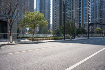 Empty urban street with asphalt road, modern high-rise buildings, and green trees in sunlight © zhu difeng