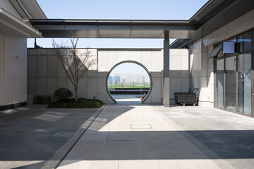 Modern courtyard with circular gate framing city skyline and distant high-rise buildings © zhu difeng