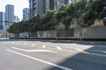 Urban road lined with green trees and modern high-rise buildings in the background © zhu difeng