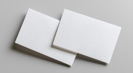 Two white, blank rectangular cards with textured surface on a plain grey backdrop, angled